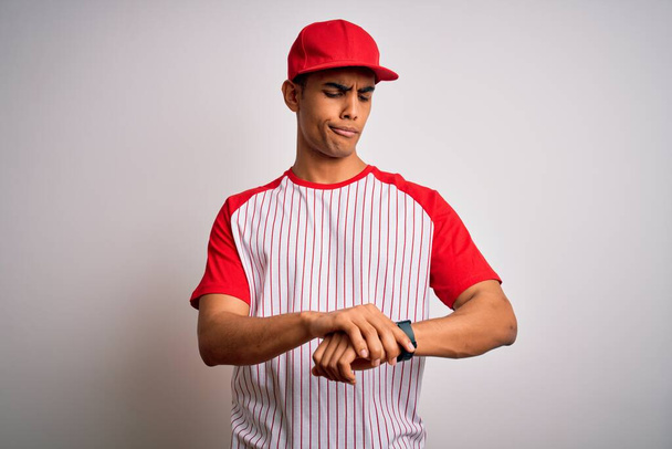 Joven deportista afroamericano guapo con camiseta y gorra de béisbol a rayas Comprobando el tiempo en el reloj de pulsera, relajado y confiado
 - Foto, imagen