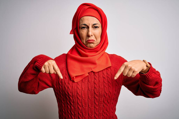 Középkorú barna nő visel muszlim hagyományos hidzsáb felett elszigetelt fehér háttér mutató lefelé néz szomorú és zaklatott, jelezve irány ujjaival, boldogtalan és depressziós. - Fotó, kép