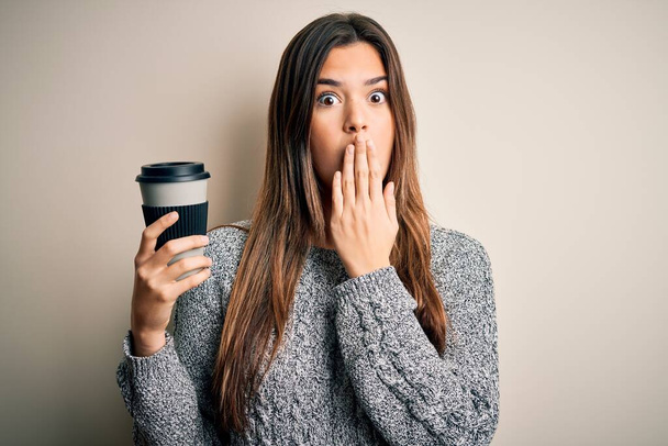 Young beautiful girl drinking cup of coffee standing over isolated white background cover mouth with hand shocked with shame for mistake, expression of fear, scared in silence, secret concept - Foto, immagini