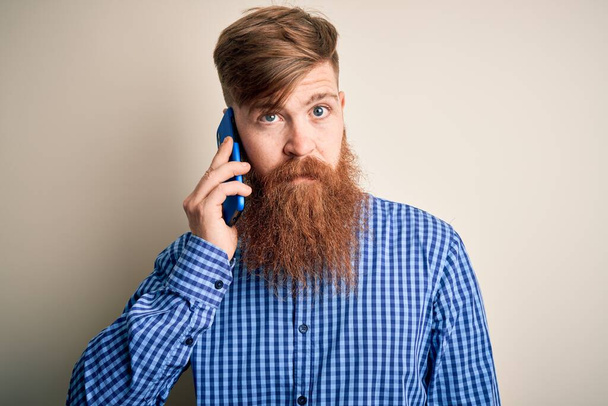 Redhead Irish man with beard having a conversation talking on smartphone over isolated background with a confident expression on smart face thinking serious - Φωτογραφία, εικόνα