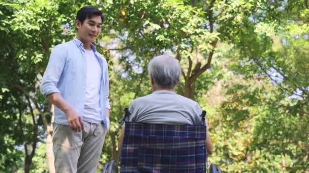 jong aziatisch zoon praten naar rolstoel gebonden gedemoraliseerd senior vader buiten - Video
