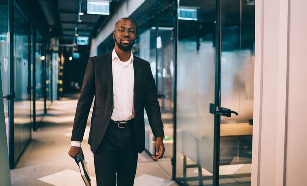 Confident African American male entrepreneur in business style clothing going with appointment book in hand on stylish modern office hall - Foto, immagini