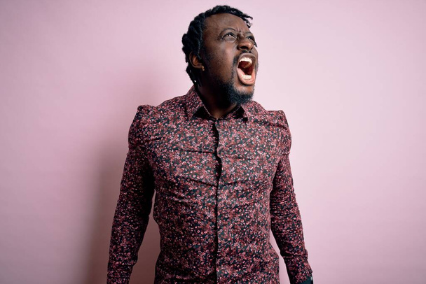 Joven hombre afroamericano guapo usando camisa casual de pie sobre fondo rosa enojado y loco gritando frustrado y furioso, gritando con ira. Rabia y concepto agresivo
. - Foto, Imagen