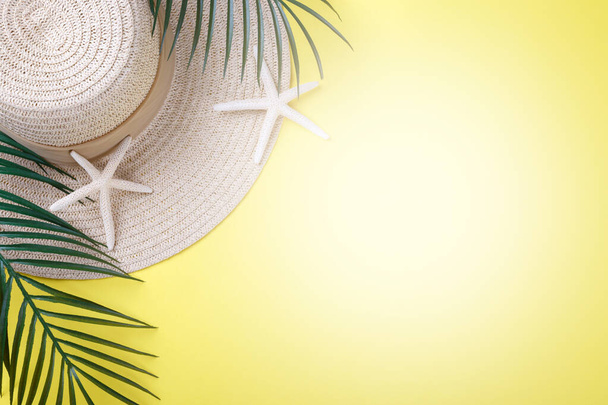 Nyári nyaralás koncepció, kalap, tengeri csillag és pálmaág sárga háttér, lapos feküdt fénymásoló hely - Fotó, kép