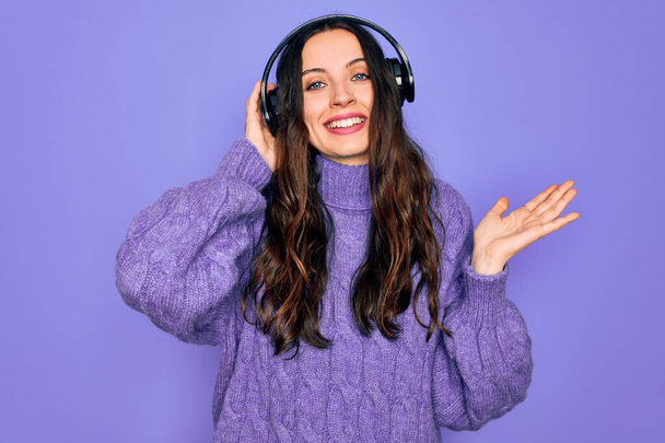 Young beautiful woman with blue eyes listening to music and dancing using headphones very happy and excited, winner expression celebrating victory screaming with big smile and raised hands - Photo, image