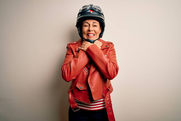 Mujer motociclista de mediana edad con casco de motocicleta y chaqueta sobre fondo blanco gritando y sofocar porque estrangulamiento doloroso. Problema de salud. Concepto de asfixia y suicidio
. - Foto, imagen