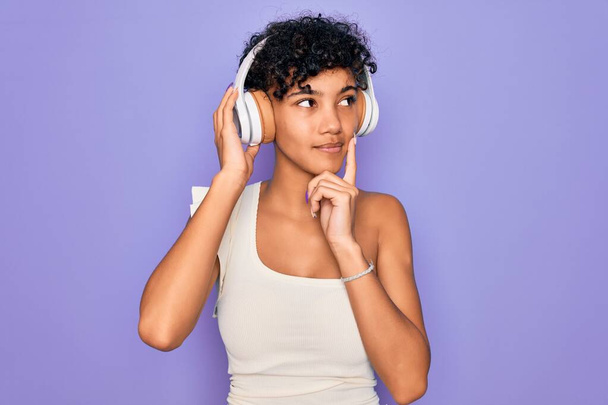 Bella donna afro-americana che ascolta musica usando cuffie su sfondo rosso faccia seria pensando alla domanda, idea molto confusa
 - Foto, immagini