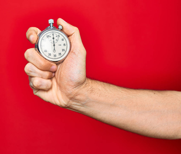 Beautiful hand of man holding stopwatch doing countdown over isolated red background - Photo, Image