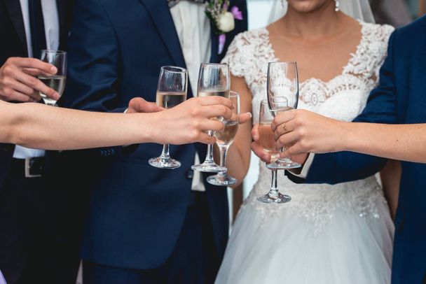 People hold in hands glasses with white wine. wedding party. friends toasting with a champagne above white table - Foto, Imagem