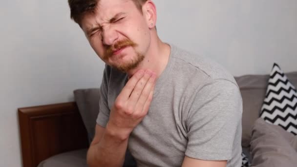 Sick unhealthy mustachioed young man touch neck hard to swallow having discomfort or painful feeling sitting on bed at home, unwell sad guy suffering from angina, sore throat, experience loss of voice - Záběry, video