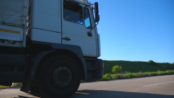 Kamera následuje kamion s nákladním přívěsem jedoucím po dálnici a převážejícím zboží za slunečného dne. Bílý náklaďák projíždí venkovskou cestou do cíle. Pomalý pohyb Boční pohled Zavřít - Záběry, video