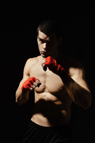 Boxeador atlético golpeando con determinación y precaución sobre fondo negro
 - Foto, Imagen