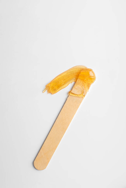 Smear of sugar paste for depilation with a wooden spatula on a white background. Spa and Shugaring. Close-up - Fotografie, Obrázek