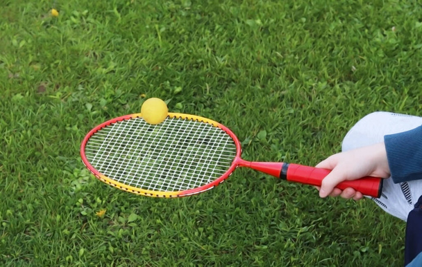 Badminton παιχνίδι με μια μπάλα στη φύση. Παιδί κατέχει ρακέτα με μπάλα στο πράσινο φόντο γρασίδι - Φωτογραφία, εικόνα