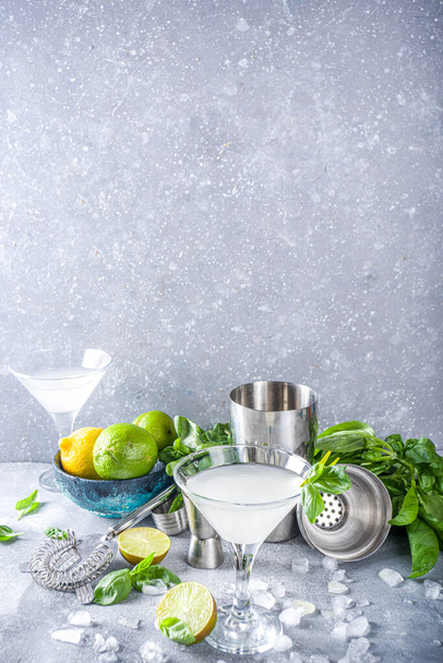 Basil vodka gimlet martini cocktail. Strong alcohol drink with fresh basil, lime and vodka in classic martini glass, Grey stone background copy space - Photo, Image