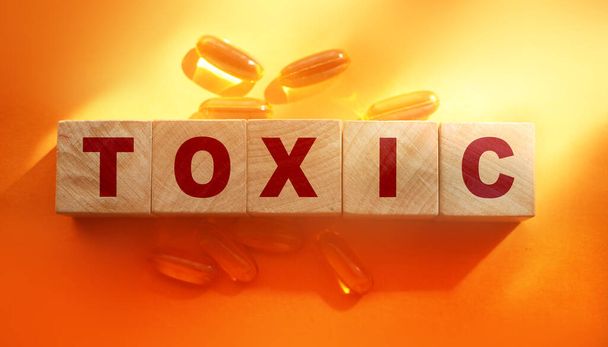 Toxic Word γραμμένο σε ξύλινους κύβους με χάπια Omega-3 γύρω. Έννοια της υγειονομικής περίθαλψης αποτοξίνωσης. - Φωτογραφία, εικόνα