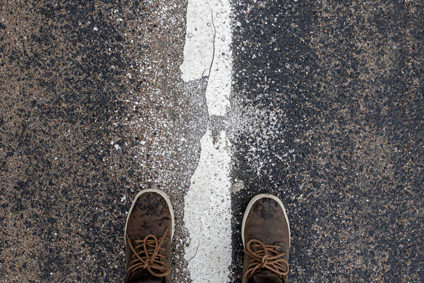 μπότες του ταξιδιώτη που στέκεται στο πεζοδρόμιο στη διαχωριστική λωρίδα. - Φωτογραφία, εικόνα