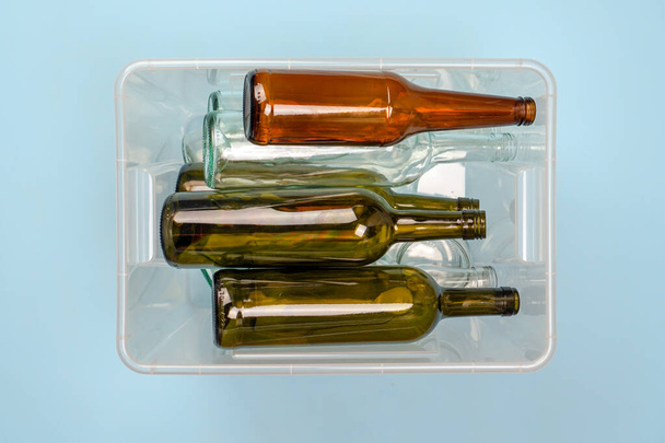 ゴミの分別。青い背景にワインとビールのガラス瓶が入った容器. - 写真・画像