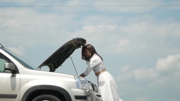 γυναίκα εκφράζει αμηχανία όταν κοιτάζει κάτω από κουκούλα του αυτοκινήτου, προβλήματα με σπασμένο αυτοκίνητό της, ανοίγοντας το καπό και καλώντας για βοήθεια στο κινητό της τηλέφωνο - Πλάνα, βίντεο