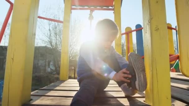 Chłopiec próbuje założyć buty na plac zabaw na świeżym powietrzu o zachodzie słońca - Materiał filmowy, wideo