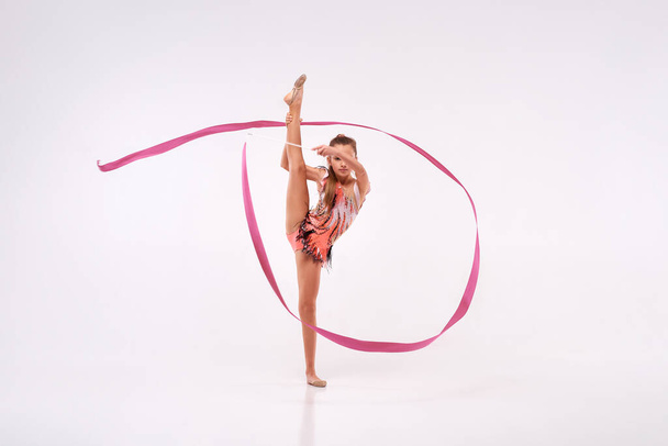 A flexible choice. Full-length shot of girl child gymnast doing acrobatic exercise using ribbon isolated on a white background. Sport, training, rhythmic gymnastics, active lifestyle concept - Fotografie, Obrázek