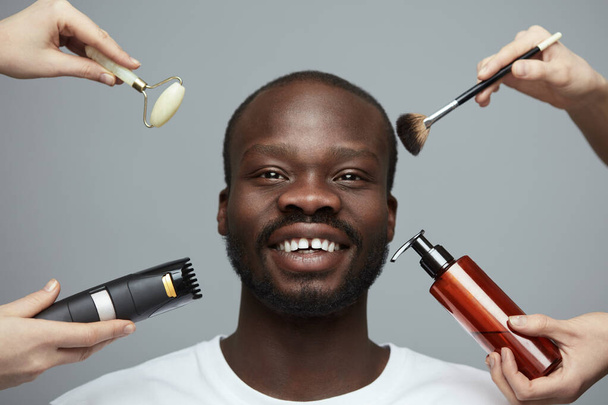 Male Skin Care. Facial Beauty Treatment For African Model. Jade Roller, Electric Razor, Makeup Brush And Liquid In Bottle Near Man's Face. - Foto, Bild