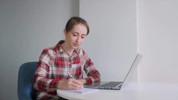 Femme utilisant un ordinateur portable, ayant un appel vidéo en ligne, prenant des notes, parlant à la maison - Séquence, vidéo