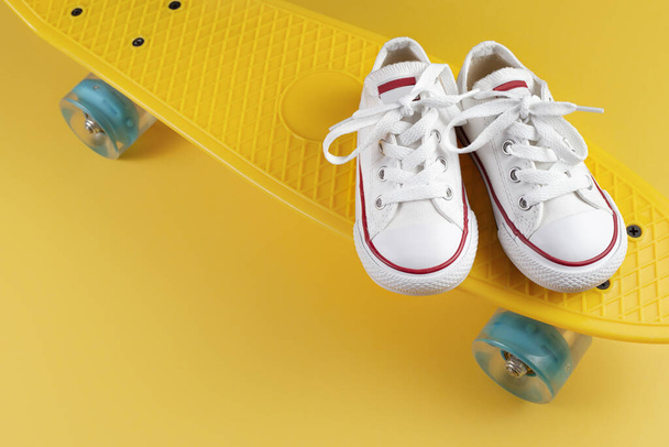 Photo of white sneakers on the skateboard or penny board over yellow background. - Fotografie, Obrázek