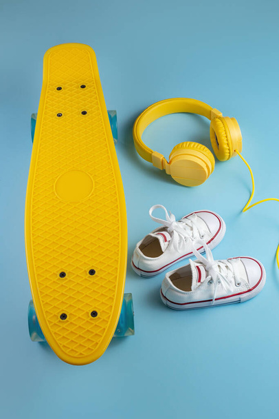 Yellow headphones, white sneakers and traditional style soccer ball over blue background. - Фото, изображение