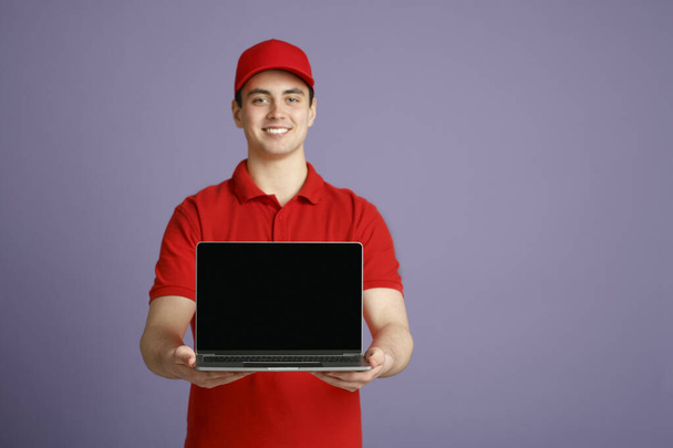 Улыбающийся курьер держит ноутбук с чистым экраном, изолированный на сером фоне, студийный снимок
 - Фото, изображение
