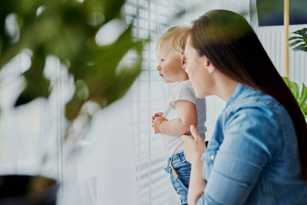 Mãe e bebê de pé ao lado da janela
 - Foto, Imagem