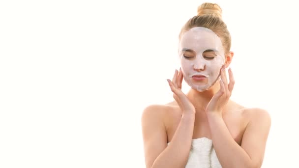 Η όμορφη γυναίκα με την καθαρή μάσκα αγγίζει το πρόσωπο στο λευκό φόντο - Πλάνα, βίντεο
