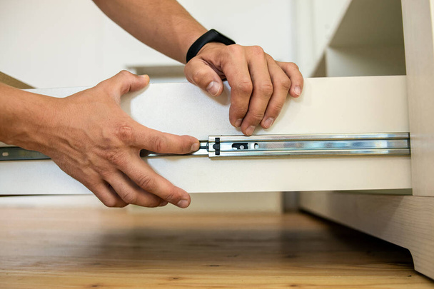 Close up of carpenter hands installing wooden drawer on sliding skids in contemporary cupboard cabinet. - Foto, Imagen