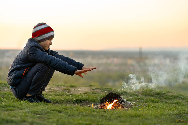 Kind jongen verwarmen in de buurt van kampvuur buiten bij koud weer. - Foto, afbeelding