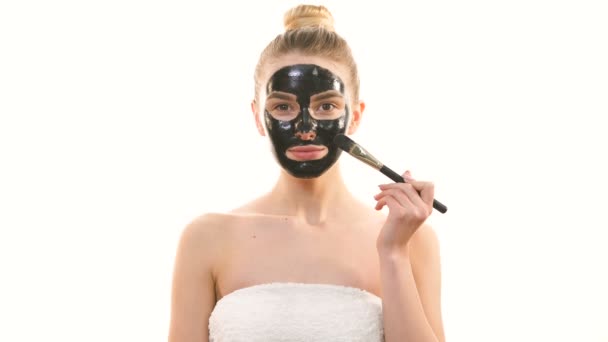 La mujer feliz aplicando una máscara negra para el cuidado de la piel sobre el fondo blanco
 - Imágenes, Vídeo