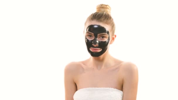A menina bonita com uma máscara de cuidado de rosto preto gesticulando no fundo branco
 - Filmagem, Vídeo