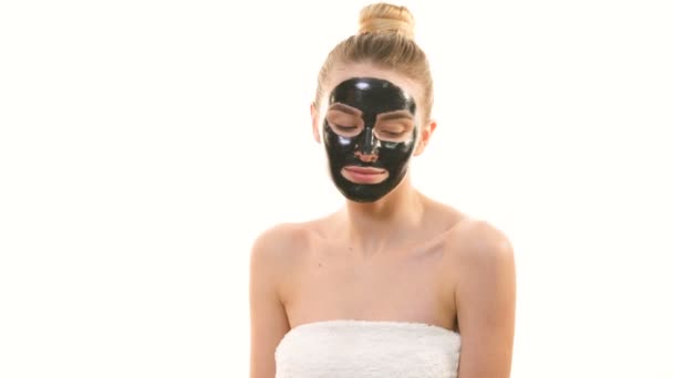Die Frau mit der schwarzen Gesichtspflegemaske gestikuliert auf weißem Hintergrund - Filmmaterial, Video