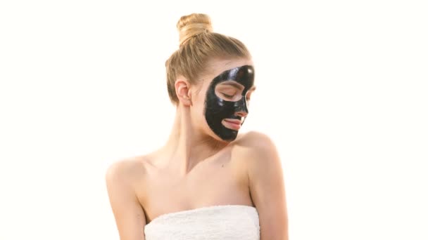 Söpö nainen, jolla on musta kasvojen hoito naamio elehtii valkoisella taustalla
 - Materiaali, video