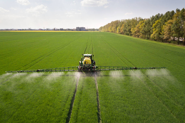 Ciągnik opryskujący wiosną pestycydy chemiczne opryskiwaczem na dużym zielonym polu rolniczym. - Zdjęcie, obraz