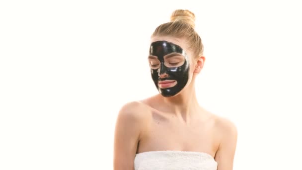 Das schöne Mädchen mit einer schwarzen Gesichtspflegemaske gestikuliert auf dem weißen Hintergrund - Filmmaterial, Video