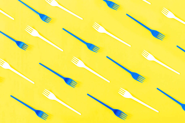 Pattern of white and blue disposable plastic forks on yellow background. Concept of environmental pollution by plastic and microplastic, waste recycling, ecology problem. Top view, flat lay. - Φωτογραφία, εικόνα