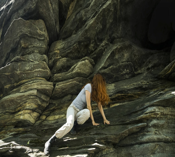 A young woman climbs on an stone wall. It`s a sunny day in the Alps. She loves the andrenaline kick. girl climbs a big stone wall. It is early in the morning, the sun is shining and the woman is wearing blue clothes.  - Foto, immagini
