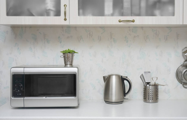 Close-up microwave and stainless electric kettle. white modern wooden table in the kitchen. - Photo, image