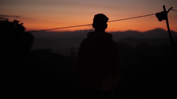 Siluetti nuoresta miehestä auringonlaskun aikaan, auringonnousu Aasiassa, Nepalissa. Vuoret, kylä
. - Materiaali, video