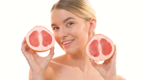 The woman holding two halves of a grapefruit on the white background - Πλάνα, βίντεο