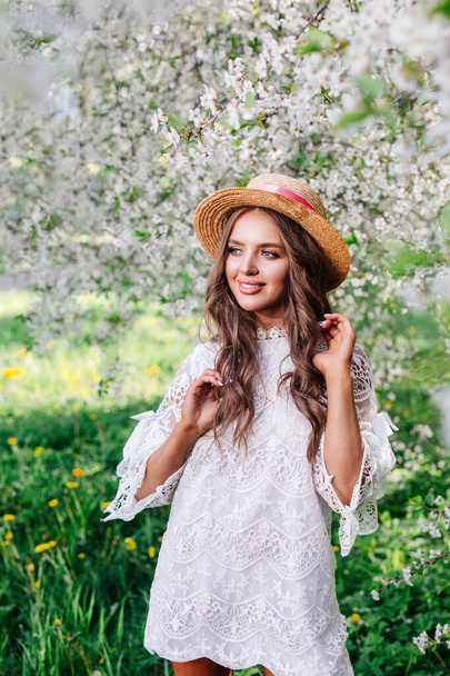 beautiful young girl in straw hat stands among the spring flowering trees. - Valokuva, kuva