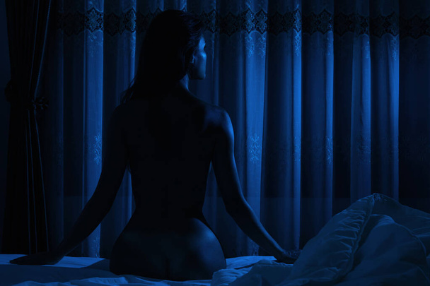 Silhouette of naked woman which sitting on the bed in the moonlight - Foto, imagen
