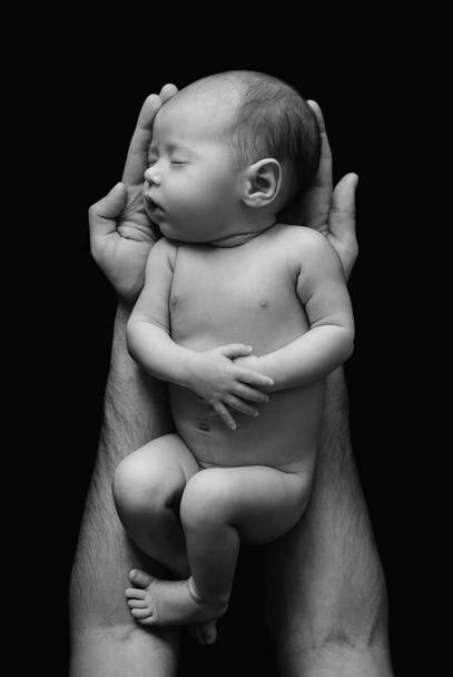 Lindo bebé recién nacido en las manos del padre sobre fondo negro
 - Foto, Imagen