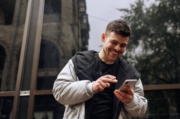 Sokakta yürüyen mutlu genç adamın portresi. Telefonuyla konuşurken yana bakıyor.. - Fotoğraf, Görsel