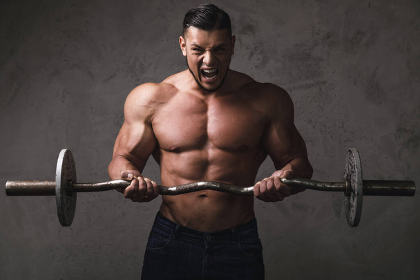 Massive brutal bodybuilder doing exercises for biceps with the barbell - Zdjęcie, obraz